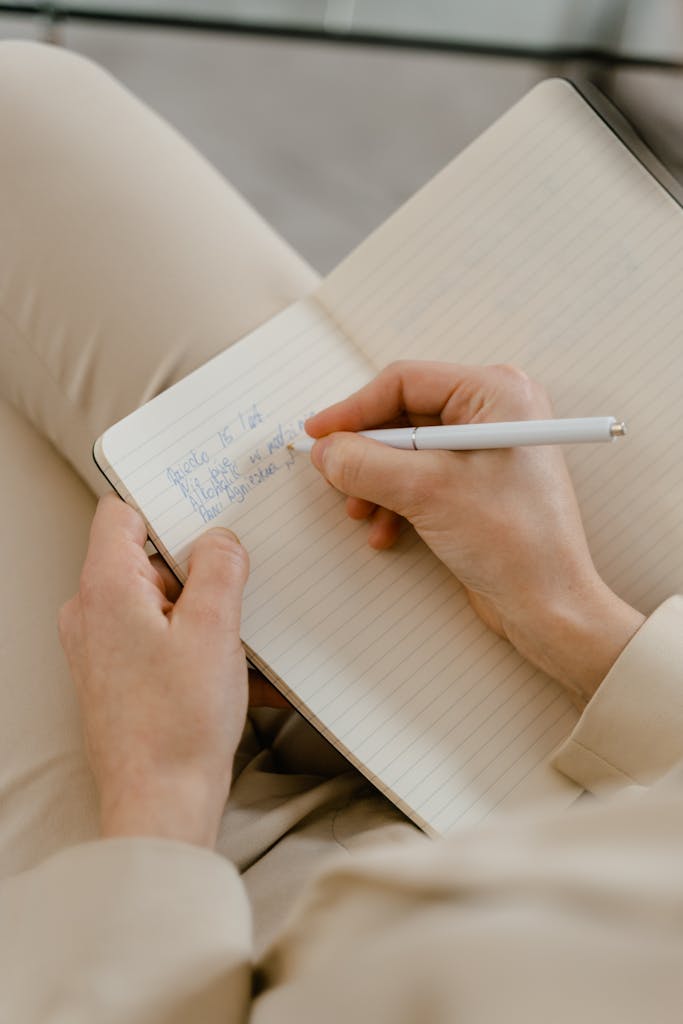 Close-up of hands writing notes in an open notebook with a pen.